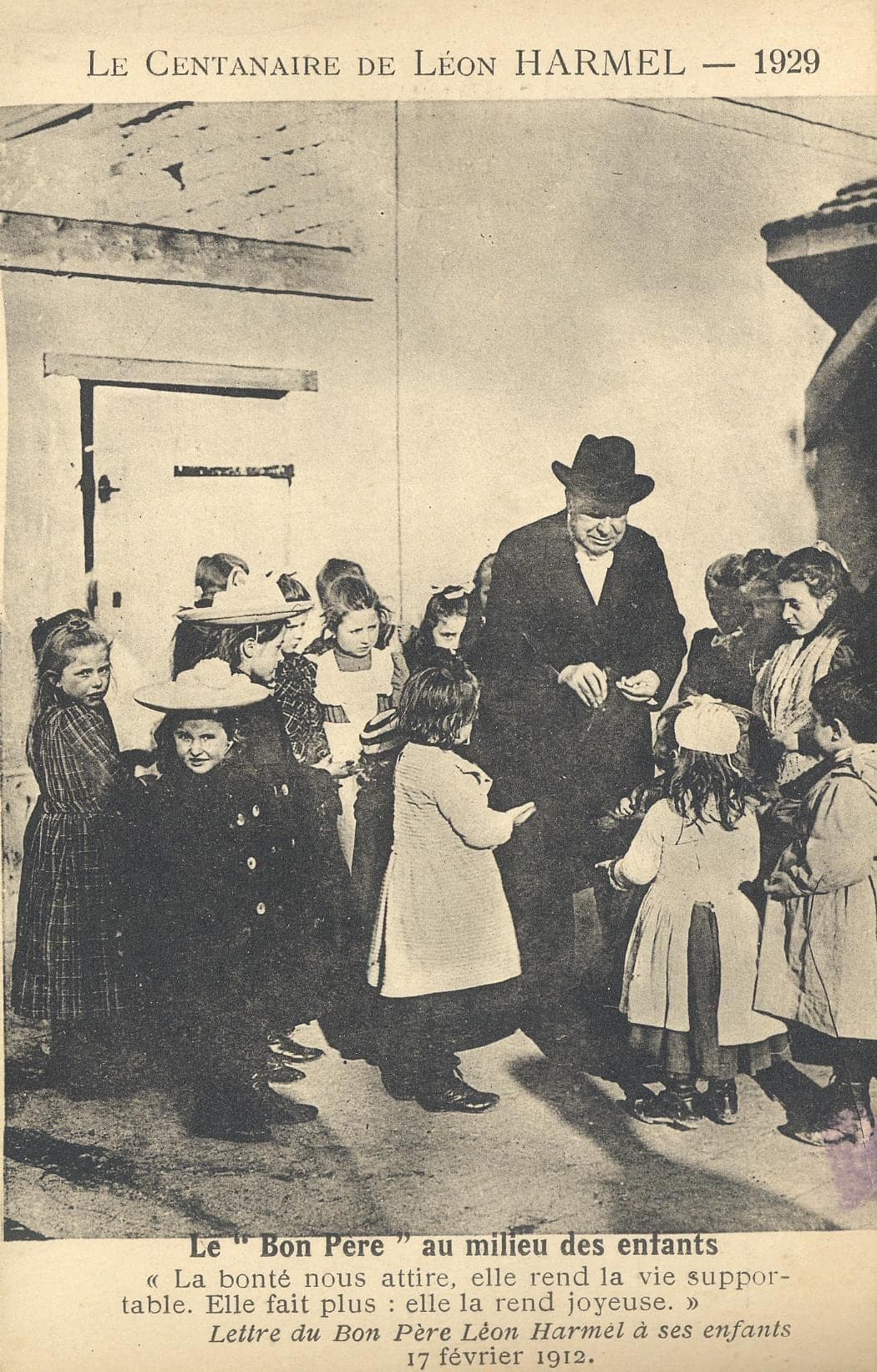 An elderly Léon Harmel in a hat, surrounded by little girls in coats and hats in a courtyard; the caption quotes his letter of 17 February 1912: “La bonté nous attire, elle rend la vie supportable. Elle fait plus : elle la rend joyeuse.” (Kindness draws us; it makes life bearable. It does more: it makes it joyful.)