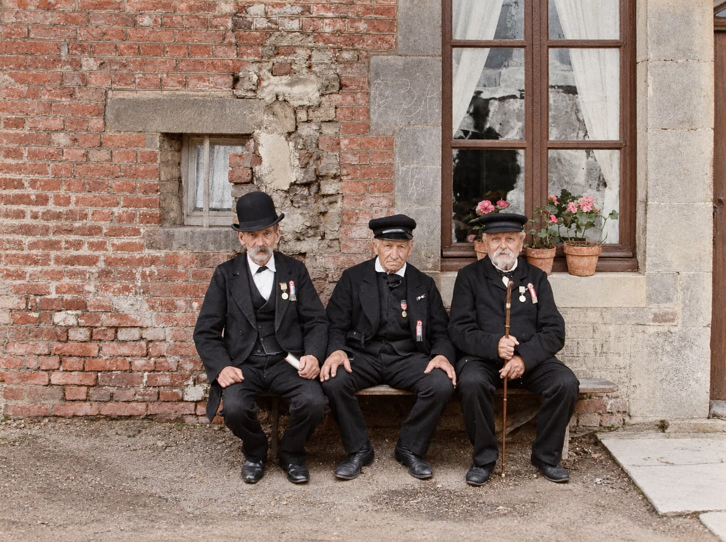 Three elderly workers sitting on a bench in front of a brick wall, each with a medal on his chest.