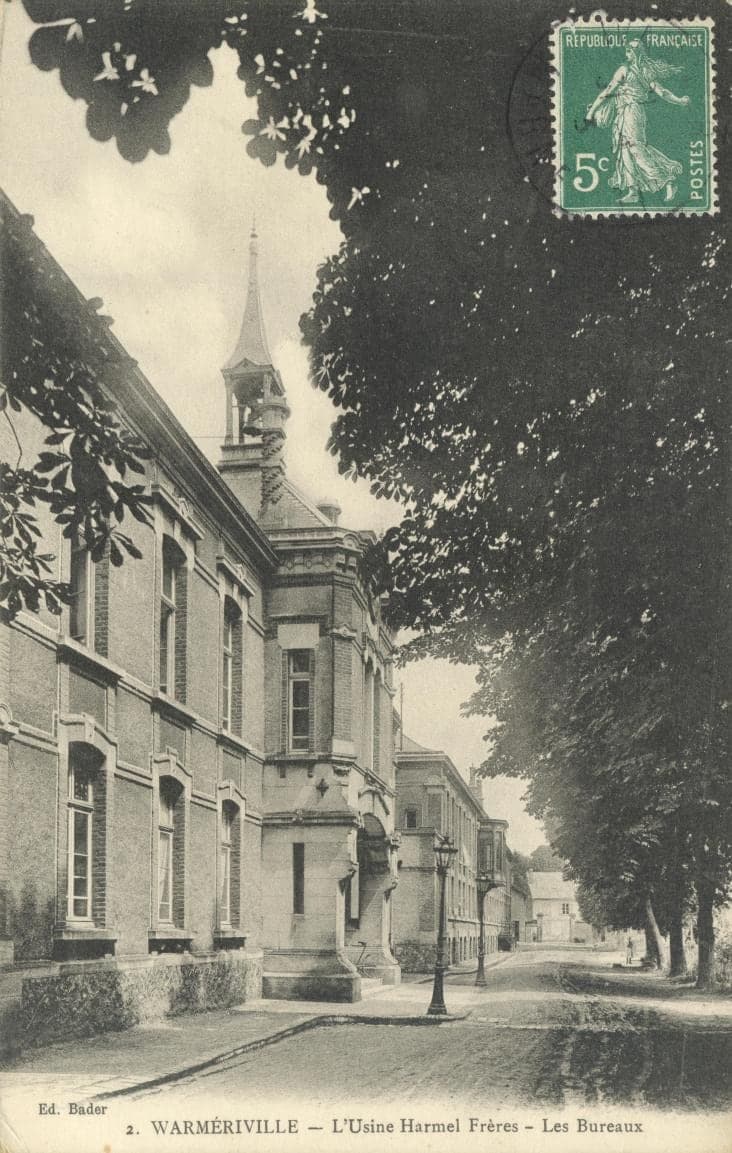 The office building and its bell turret seen along an avenue lined with tall trees and street lamps.