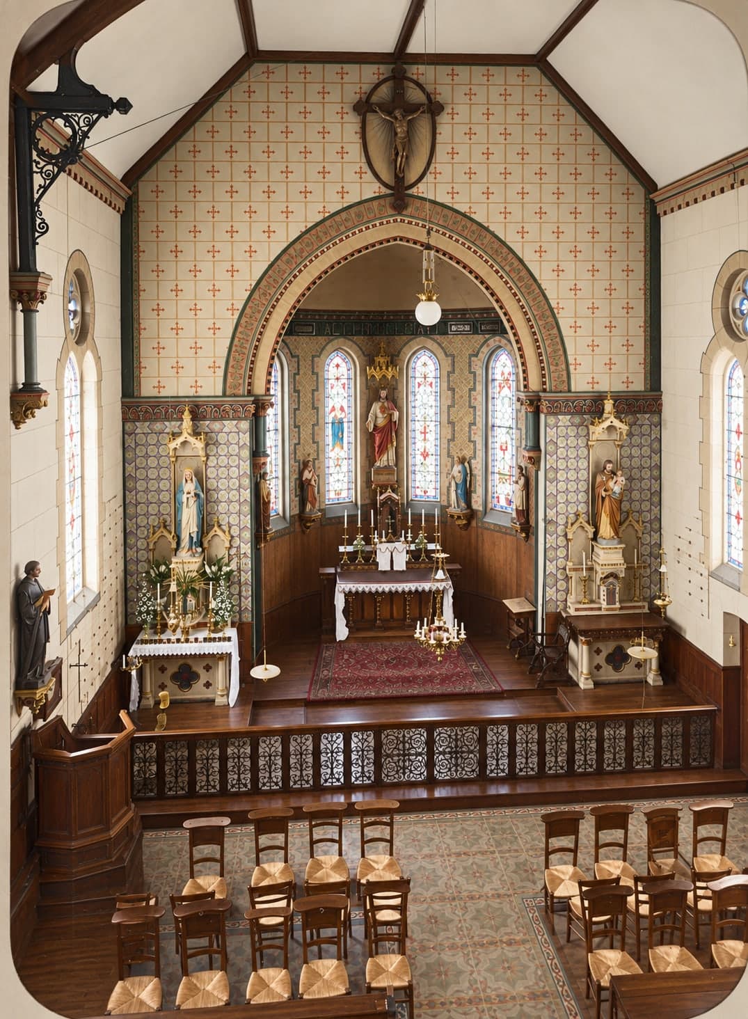 A nave with rush-seated chairs leading to the apsidal choir lit by stained-glass windows; high altar, hanging crucifix and side altars, one of them with a Virgin and Child.