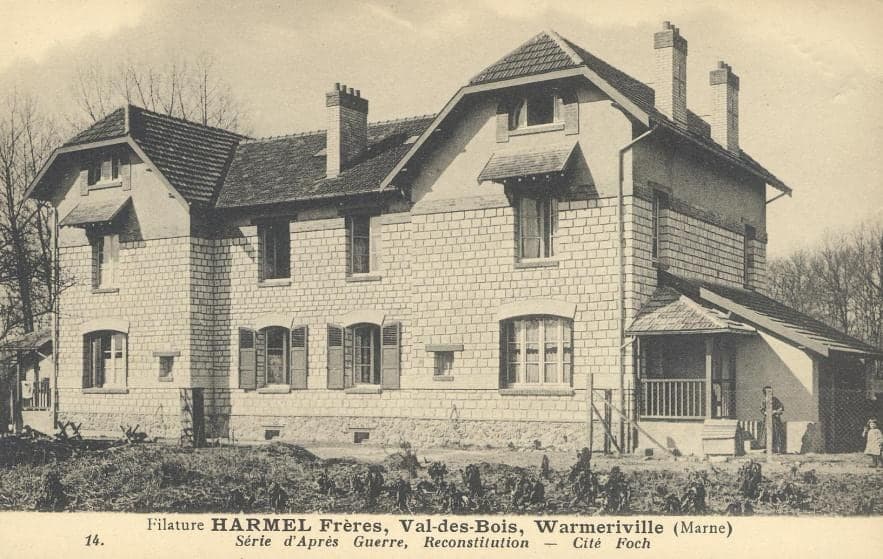 A semi-detached workers' house rebuilt after the war, in rubble stone, with hooded dormers and a veranda, in front of a garden.