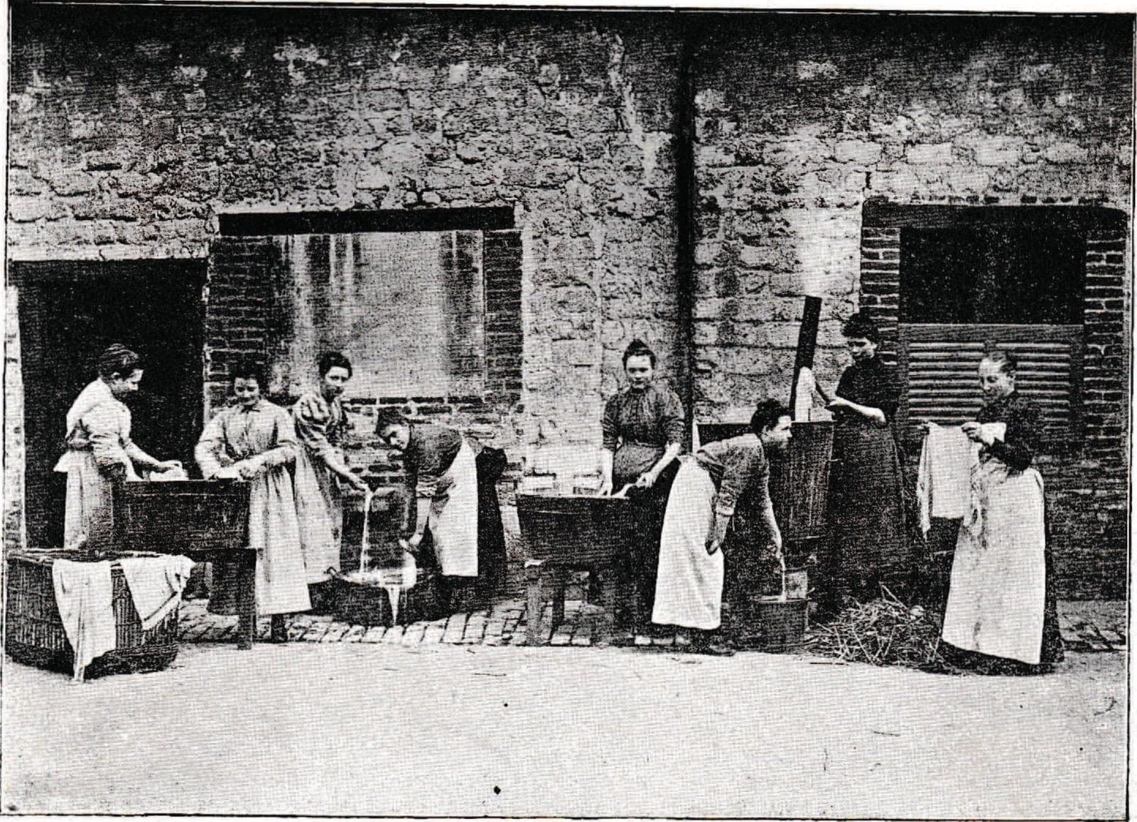 In a courtyard, girls in aprons do the washing in wooden tubs before a wall of stone and brick; linen dries over a basket.