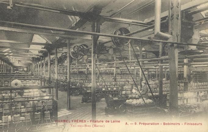 The combed-wool preparation workshop: machines in a long line, pulleys and belts, piles of bobbins in the foreground.