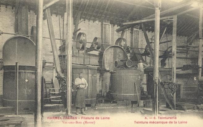 Large cylindrical vats for mechanical dyeing, linked to pulleys in the ceiling; a worker in an apron poses in the centre.