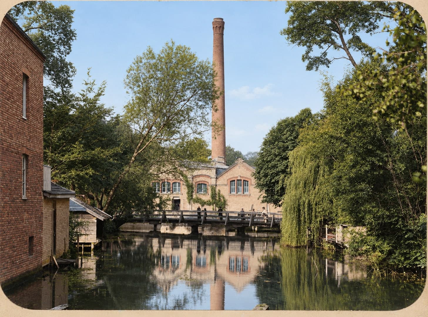 The tree-lined Suippe, a footbridge, and in the background the mill buildings dominated by a very tall chimney.