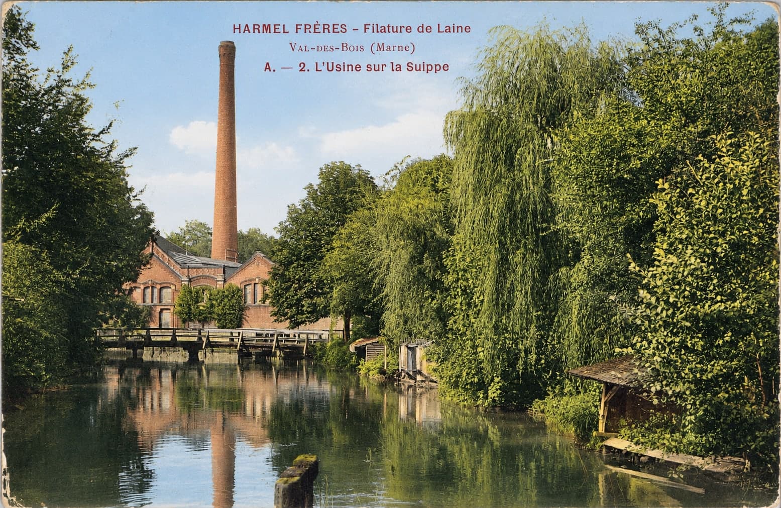 The Suippe lined with willows, a footbridge, and in the background the mill buildings dominated by the tall chimney.