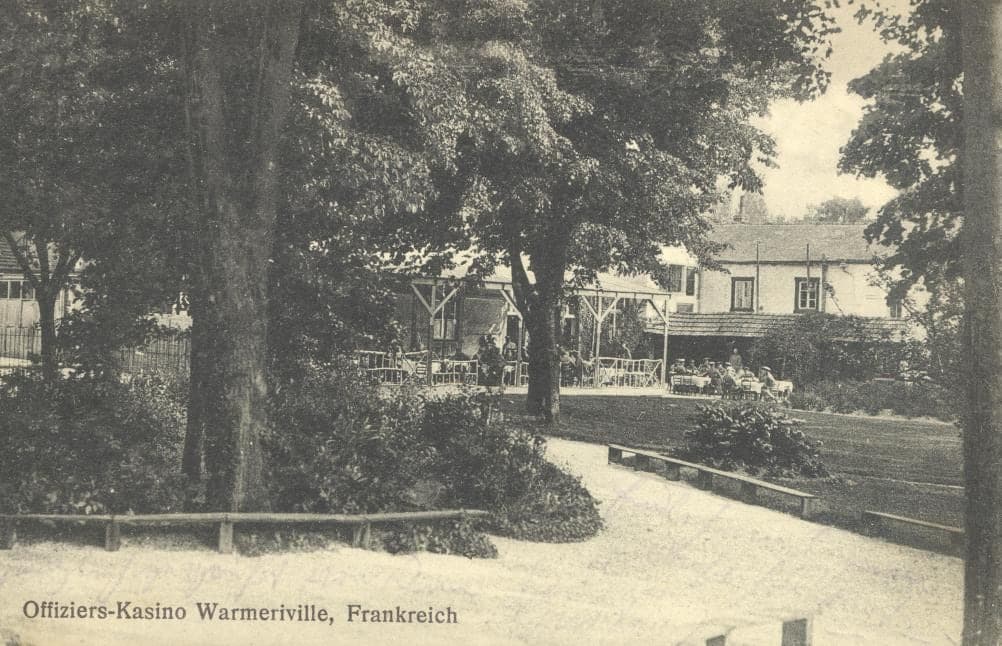 The garden of the German officers' mess in Warmeriville: paths, lawn and tall trees, a house in the background.